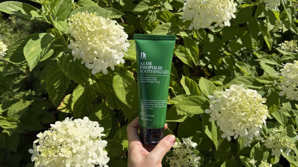 Gel calmant cu aloe și propolis de la Benton, ținut în mână, pe fundal natural cu flori albe