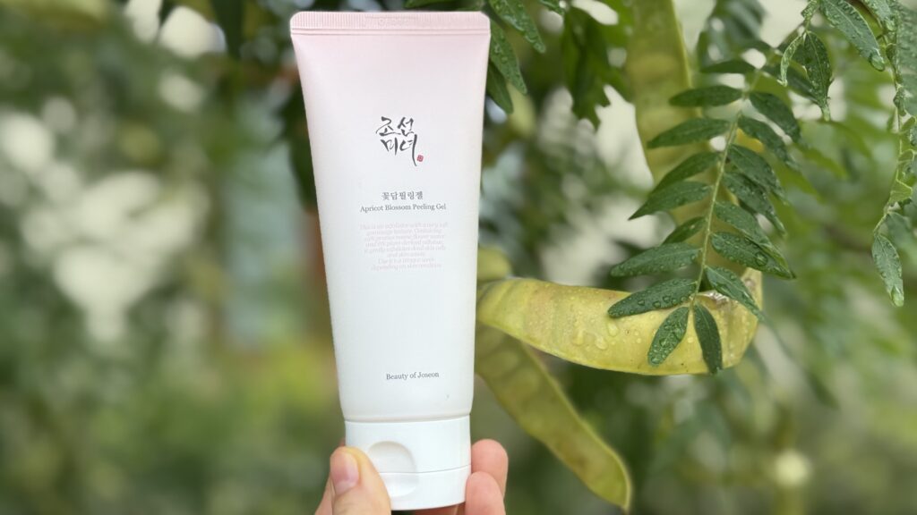 Beauty of Joseon Apricot Blossom Peeling Gel – produs exfoliant delicat, fotografiat pe fundal natural cu frunze verzi ude, pentru îngrijirea buzelor și a pielii iarna.