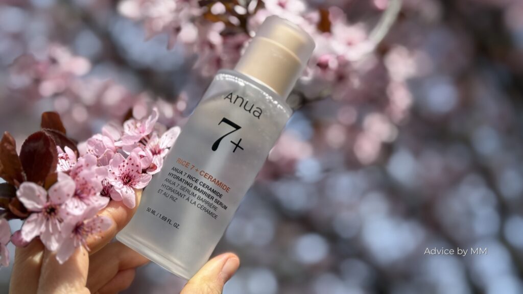 Anua 7 Rice Ceramide Hydrating Barrier Serum ținut în mână, fotografiat în lumină naturală pe fundal de flori roz.