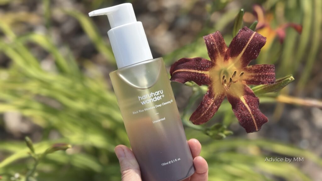 Haruharu Wonder Black Rice Moisture Deep Cleansing Oil ținut în mână, fotografiat în lumină naturală lângă o floare vișinie.
