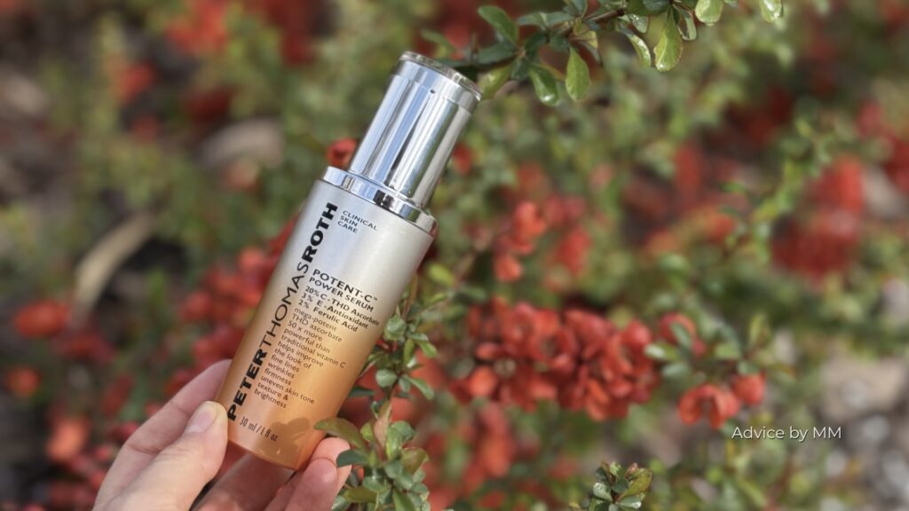 Ser Peter Thomas Roth Potent-C Power Serum fotografiat în lumină naturală, între flori roșii; produs cosmetic care conține phenoxyethanol.