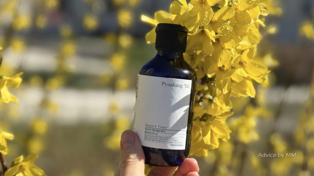 Pyunkang Yul Essence Toner fotografiat în fața unor flori galbene de primăvară. Produsul conține Bis-PEG-18 Methyl Ether Dimethyl Silane, un silicon hidrosolubil utilizat pentru îmbunătățirea texturii și hidratării pielii.